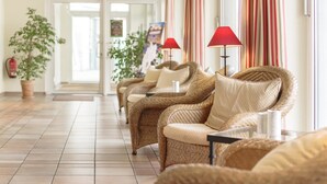 A row of wicker chairs with red lamps, a tiled floor, and a plant in the background. - Hotel Leipzig City Nord by Campanile (Leipzig)
