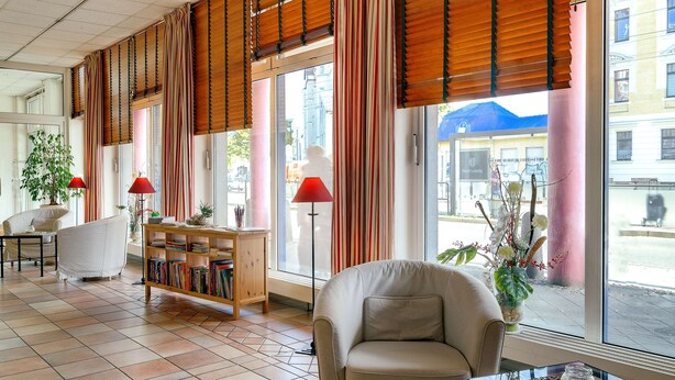A hotel lobby with a sofa, a bookshelf, a coffee table, and large windows with curtains. - Hotel Leipzig City Nord by Campanile (Leipzig)