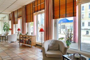 A hotel lobby with a sofa, a bookshelf, a coffee table, and large windows with curtains. - Hotel Leipzig City Nord by Campanile (Leipzig)