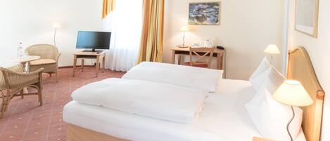 A hotel room with a bed, a desk with a computer, a chair, a TV, and a painting on the wall.
