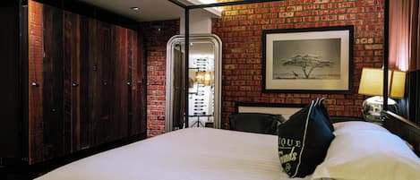 Una habitación de hotel con pared de ladrillo, una cama grande, un armario y un cuadro enmarcado en la pared.
