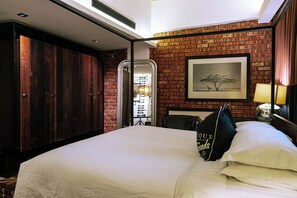A hotel room with a brick wall, a large bed, a wardrobe, and a framed picture on the wall.