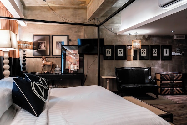 A modern hotel room with a large bed, a desk with a flat-screen TV, a leather armchair, and a small table.