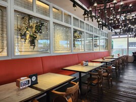 A restaurant interior with long tables, red cushioned seating, and decorative hanging lights.