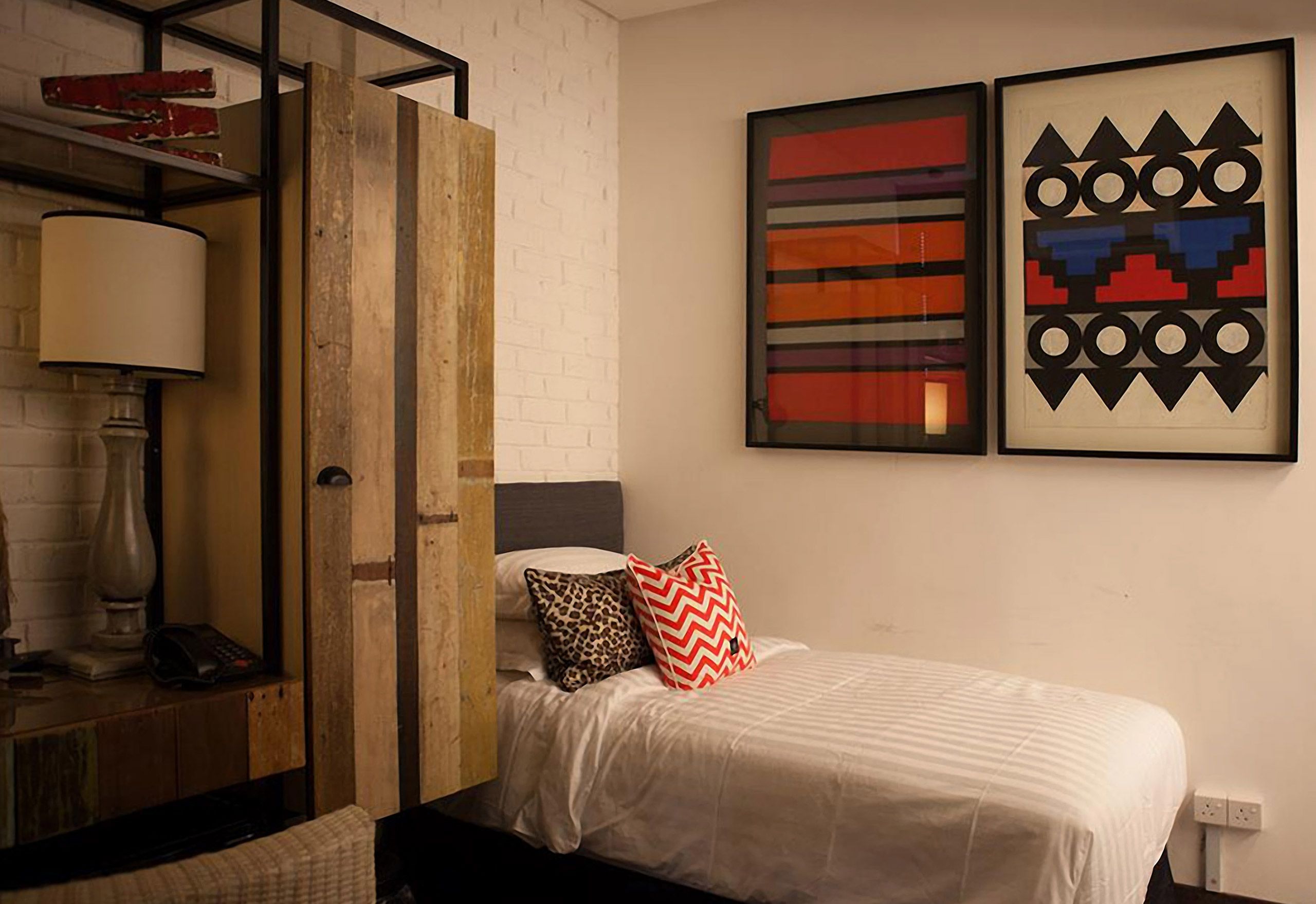 A bedroom with a bed, a nightstand, a lamp, and two abstract paintings on the wall.