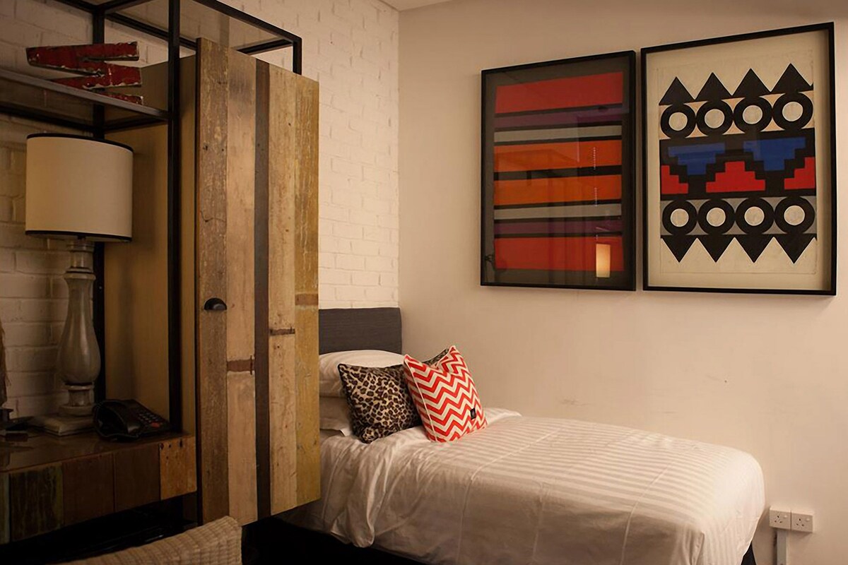 A bedroom with a bed, a nightstand, a lamp, and two abstract paintings on the wall.