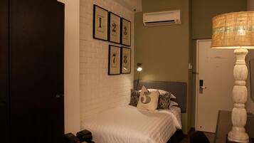 Un dormitorio con pared de ladrillo blanco, cama con cabecera, lámpara y puerta.