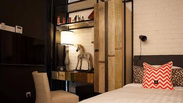 A hotel room with a bed, a chair, a wooden shelf with a horse statue, a lamp, and a television.