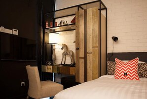 A hotel room with a bed, a chair, a wooden shelf with a horse statue, a lamp, and a television.