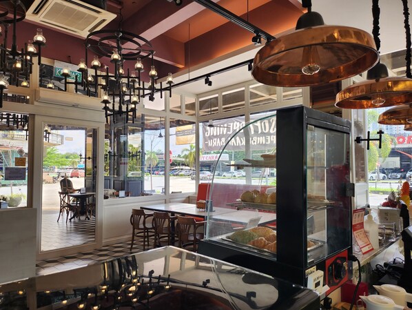 A bakery with a display case of pastries, a seating area with tables and chairs, and a view of the street outside.