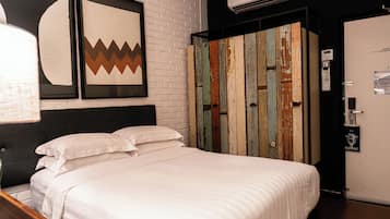 A neatly made bed with white linens in a room with a brick wall and a colorful wooden wardrobe.