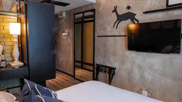 A hotel room with a bed, a TV mounted on the wall, a wooden floor, and a door leading to another room.