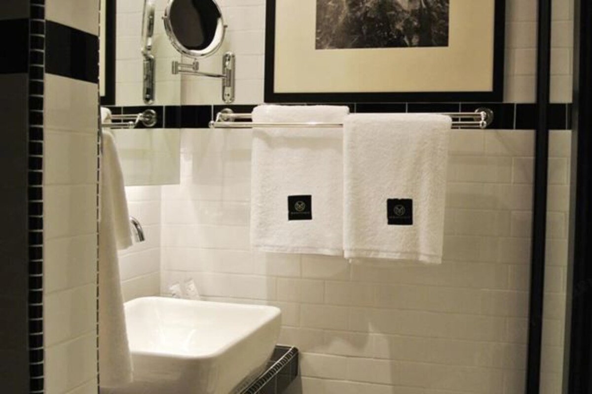 A bathroom with a white sink, two white towels, a mirror, and a framed picture on the wall.