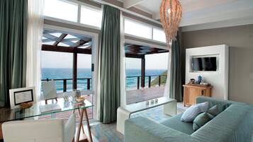 Una sala de estar moderna con un amplio ventanal con vistas al mar, una mesa de vidrio, un sofá y un televisor montado en la pared.
