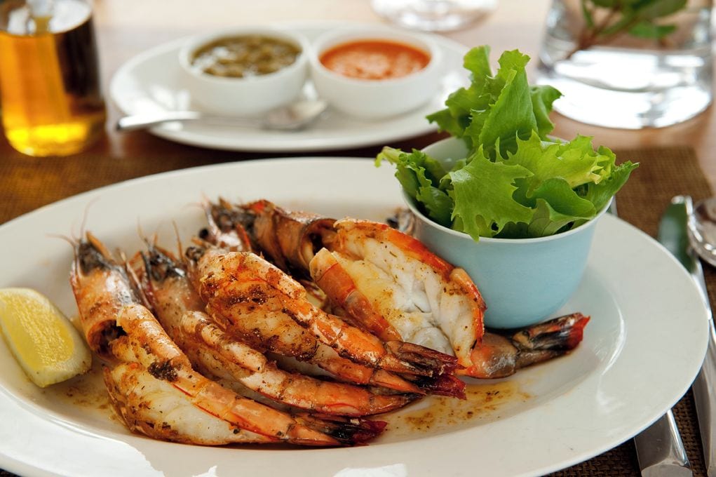 Un plato de camarones cocidos con gajos de limón y un pequeño bol de vegetales verdes.