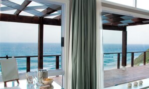 A room with a view of the ocean, a table with a painting, and a window with curtains. - White Pearl Resorts (Zitundo)