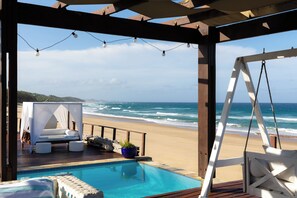 A beachside pool area with a cabana, lounge chairs, and a view of the ocean. - White Pearl Resorts (Zitundo)