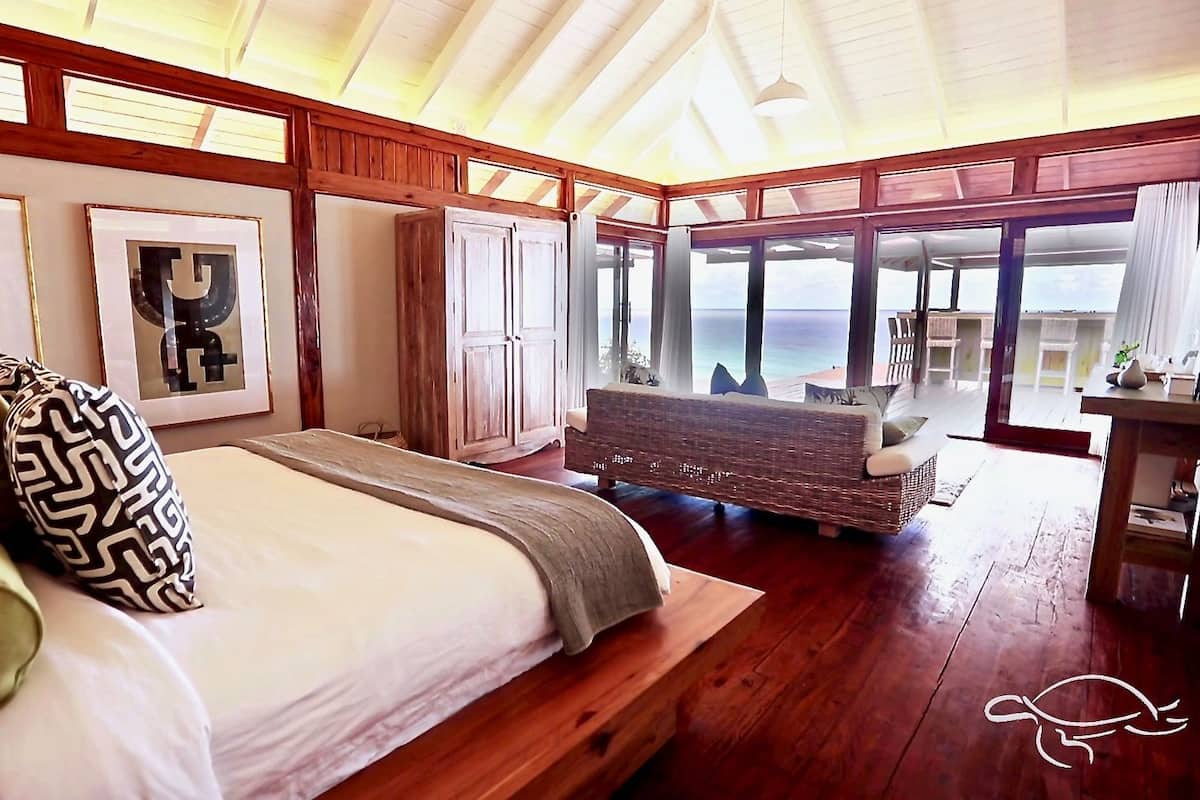 Ein Schlafzimmer mit einem großen Bett, Holzboden, einem Schreibtisch und Meerblick.