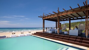A poolside area with a wooden pergola, lounge chairs, and a view of the beach and ocean. - White Pearl Resorts (Zitundo)