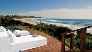 A wooden deck with a white sofa and a pool, overlooking a beach with waves and a clear sky. - White Pearl Resorts (Zitundo)