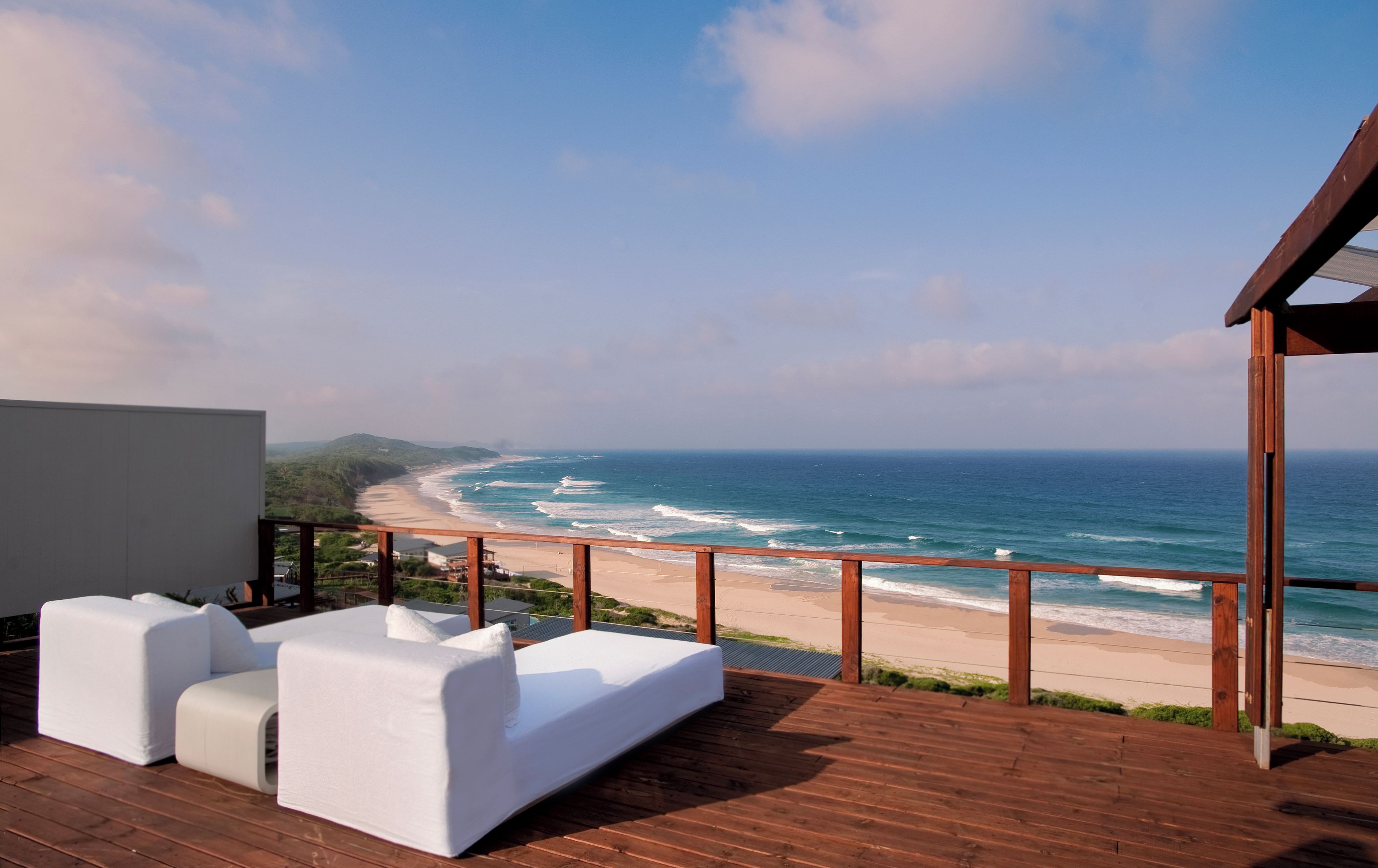 Een houten terras met een witte bank en uitzicht op het strand en de oceaan.