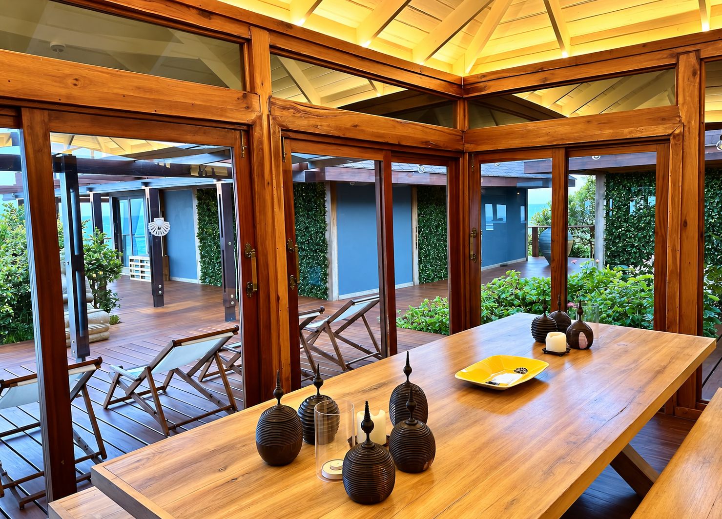 Una mesa de comedor de madera con velas y jarrones, rodeada de puertas de cristal que dan a un jardín.