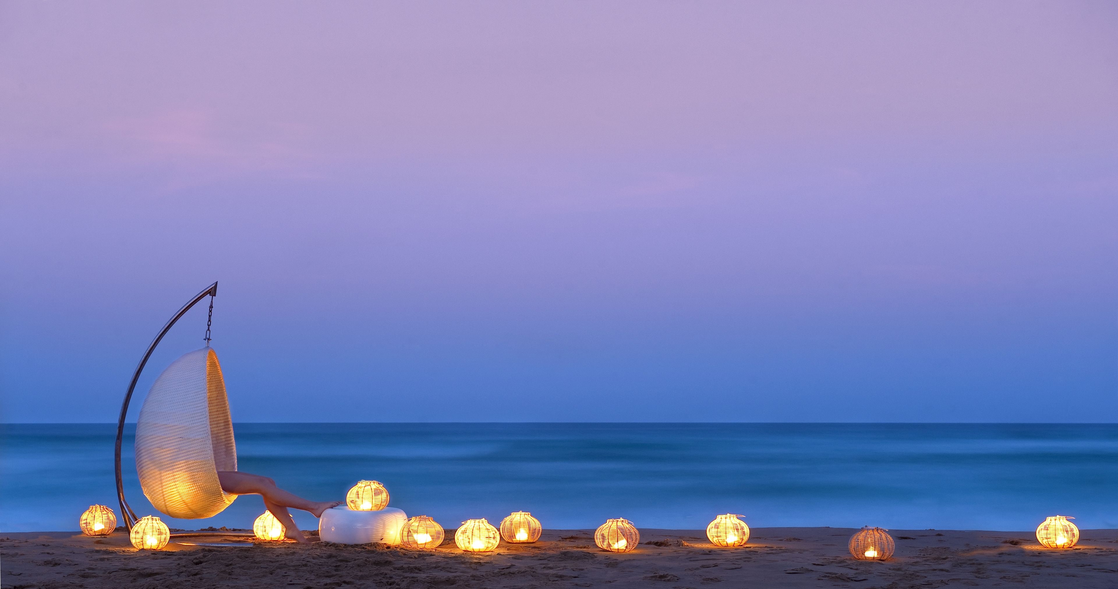 Escena de playa con una silla hamaca y varios faroles encendidos.
