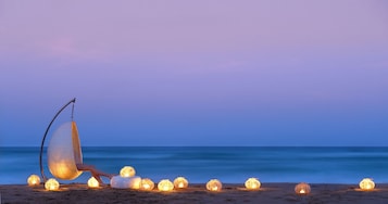 Escena de playa con una silla hamaca y varios faroles encendidos.