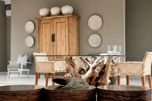 A dining area with a glass-top table, wooden chairs, a wooden cabinet, and decorative plates on the wall. - White Pearl Resorts (Zitundo)