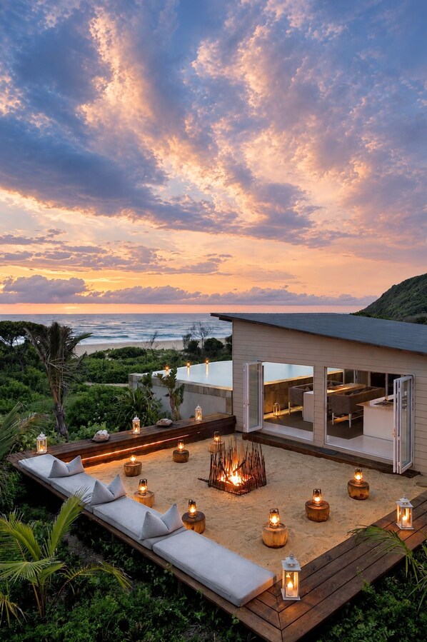 A beachfront property with a modern outdoor seating area, a fire pit, and a view of the ocean.