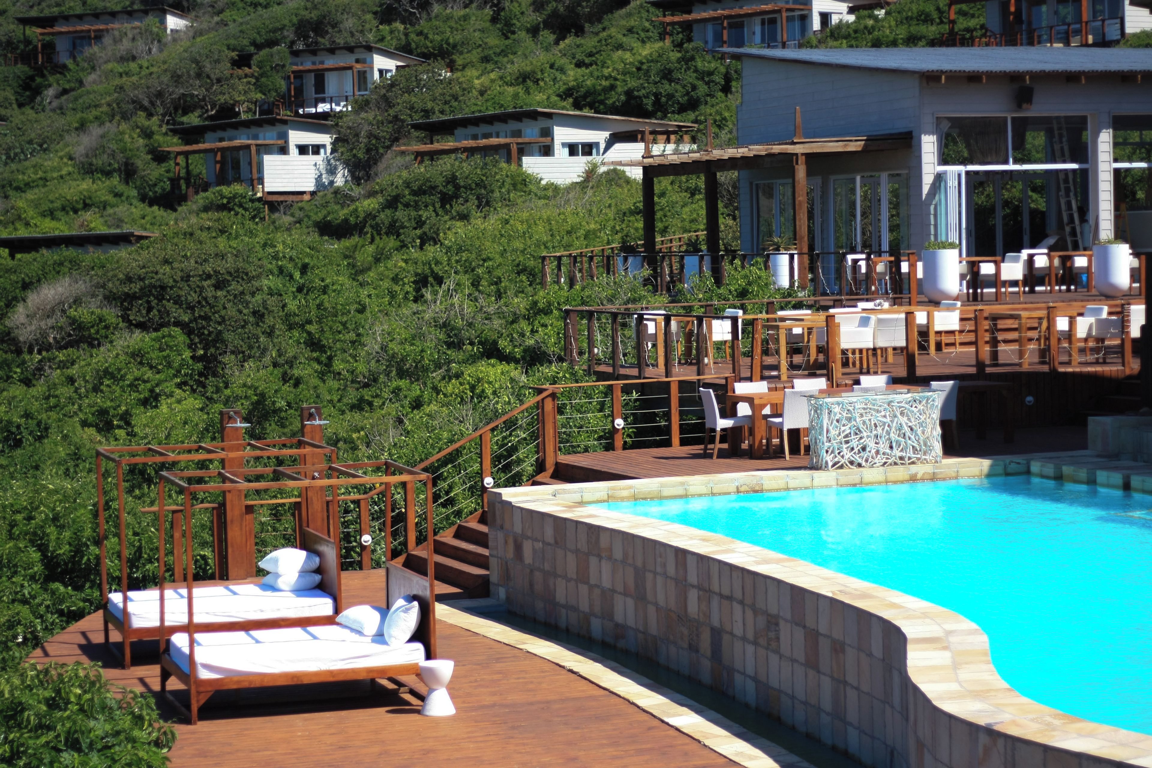 A pool area with a wooden deck, lounge chairs, and a stone wall.