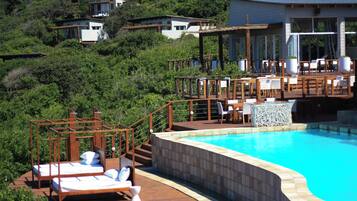 A pool area with a wooden deck, lounge chairs, and a stone wall.