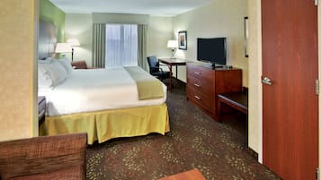 A hotel room with a large bed, a desk with a television, a chair, and a dresser.