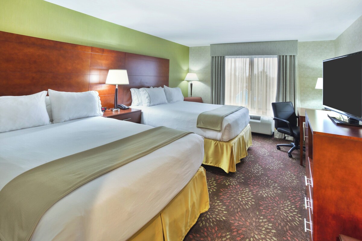 A hotel room with two beds, a desk, a television, and a window with curtains.