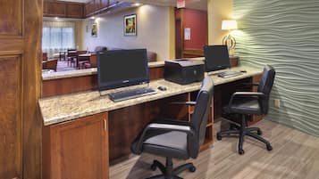 A hotel business center with two desktop computers, a printer, and office chairs.
