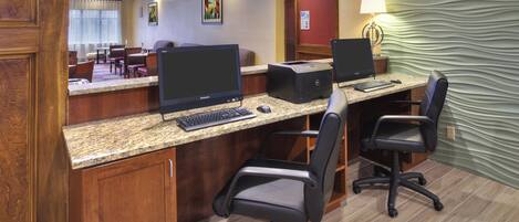 A hotel business center with two desktop computers, a printer, and office chairs.