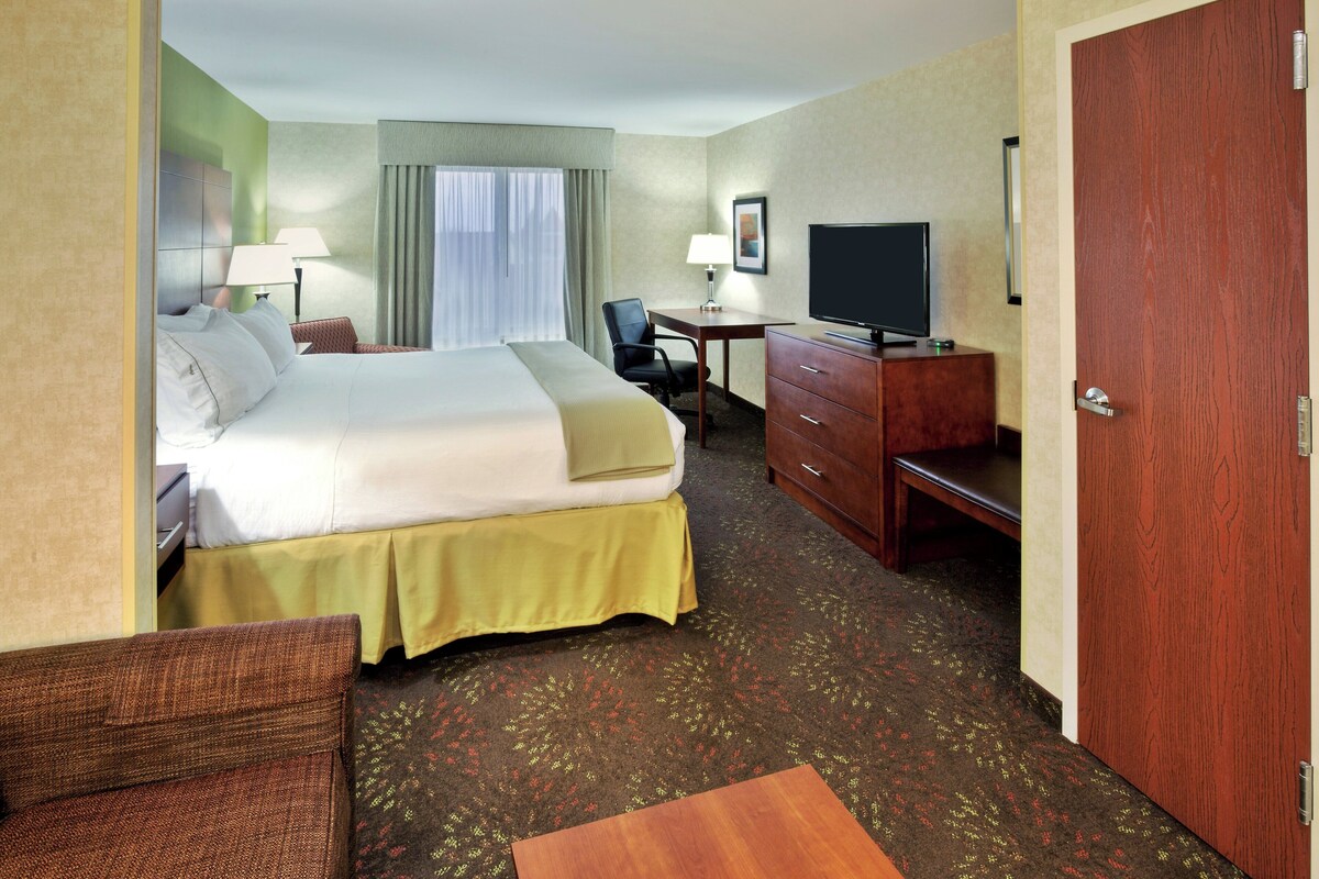 A hotel room with a bed, desk, television, and a door.