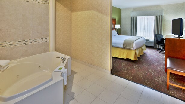 A hotel room with a large bathtub, a bed with a yellow bedspread, a desk with a computer, and a television. - Holiday Inn Express Hotel & Suites Frankenmuth by IHG (Frankenmuth)
