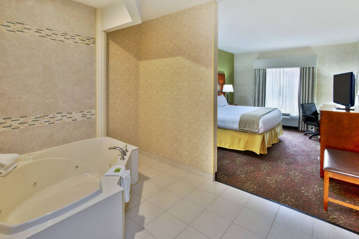 A hotel room with a large bathtub, a bed with a yellow bedspread, a desk with a computer, and a television.