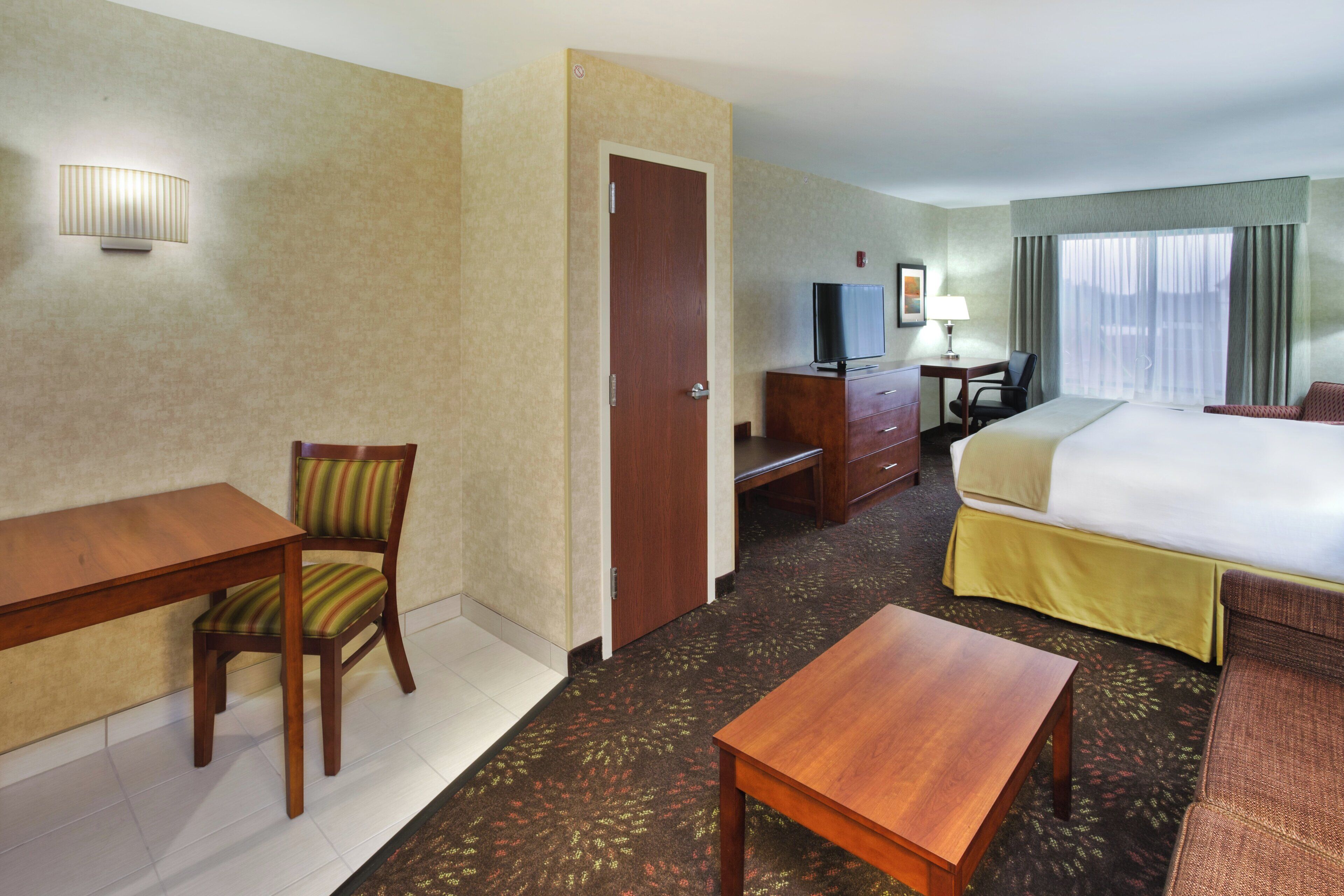 Ein Hotelzimmer mit Bett, Schreibtisch, Stuhl, Fernseher und Lampe.