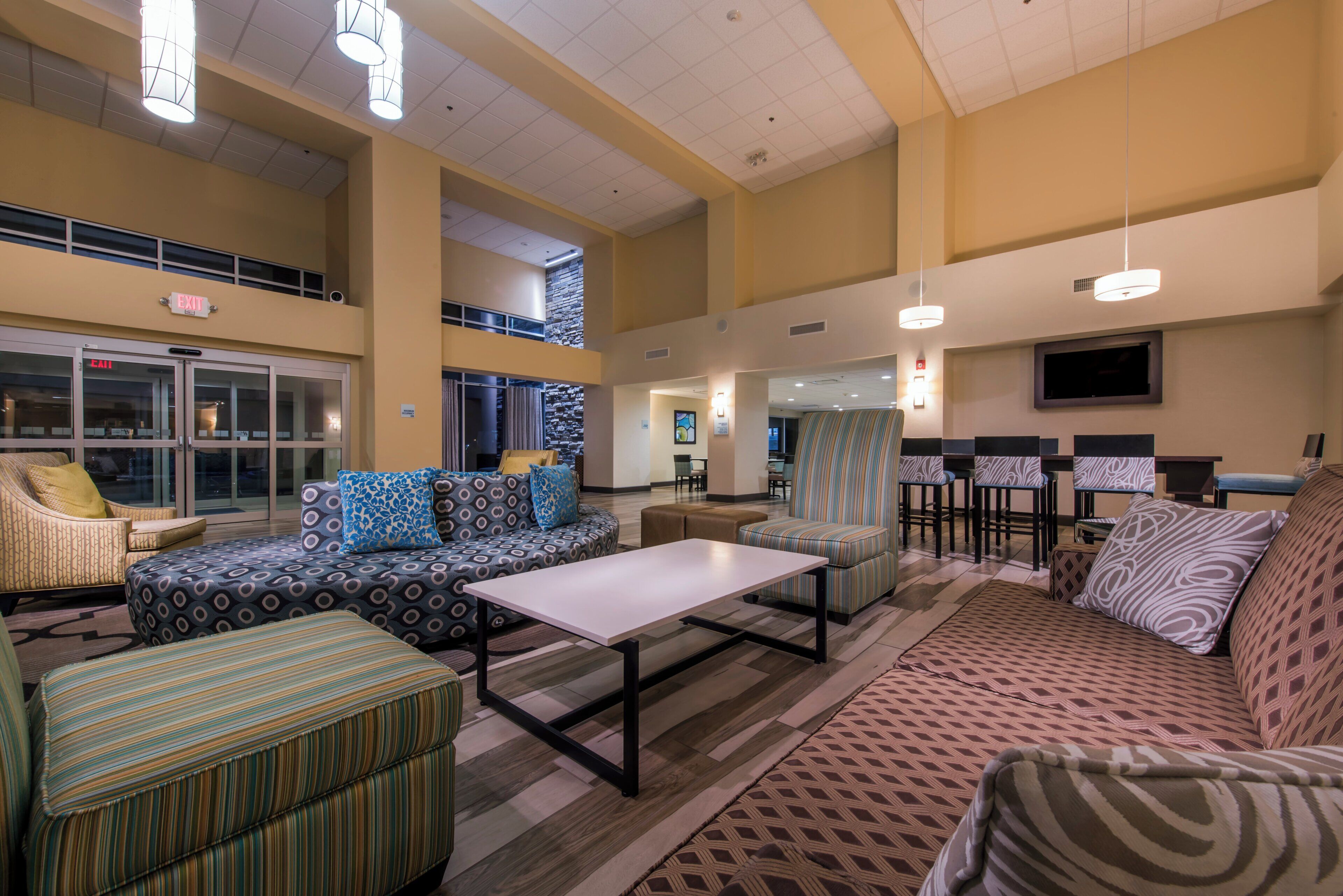 A spacious lobby with seating areas, a flat-screen TV mounted on the wall, and an exit sign above the door.