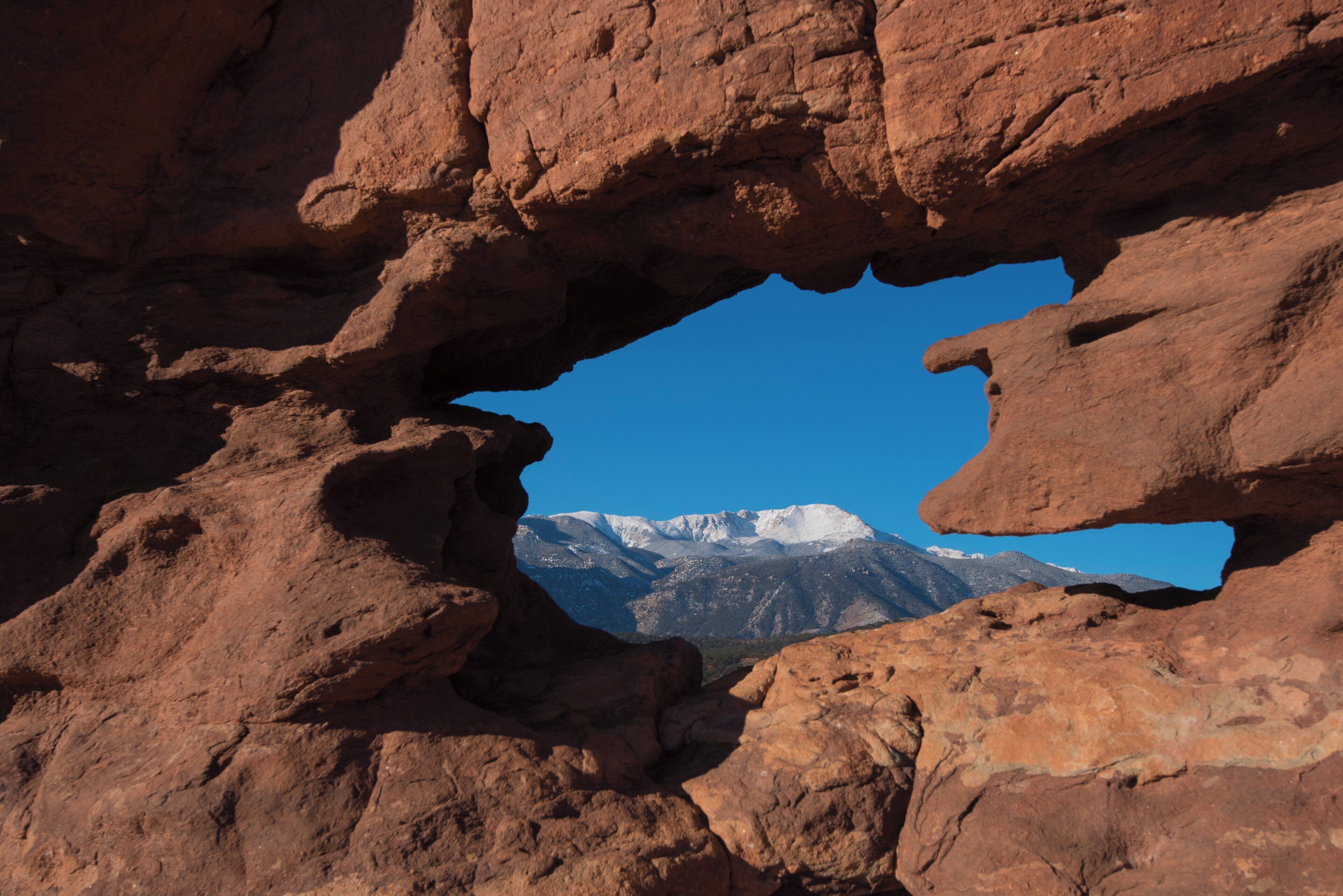 A natural rock formation with a clear view of snow-capped mountains in the background.