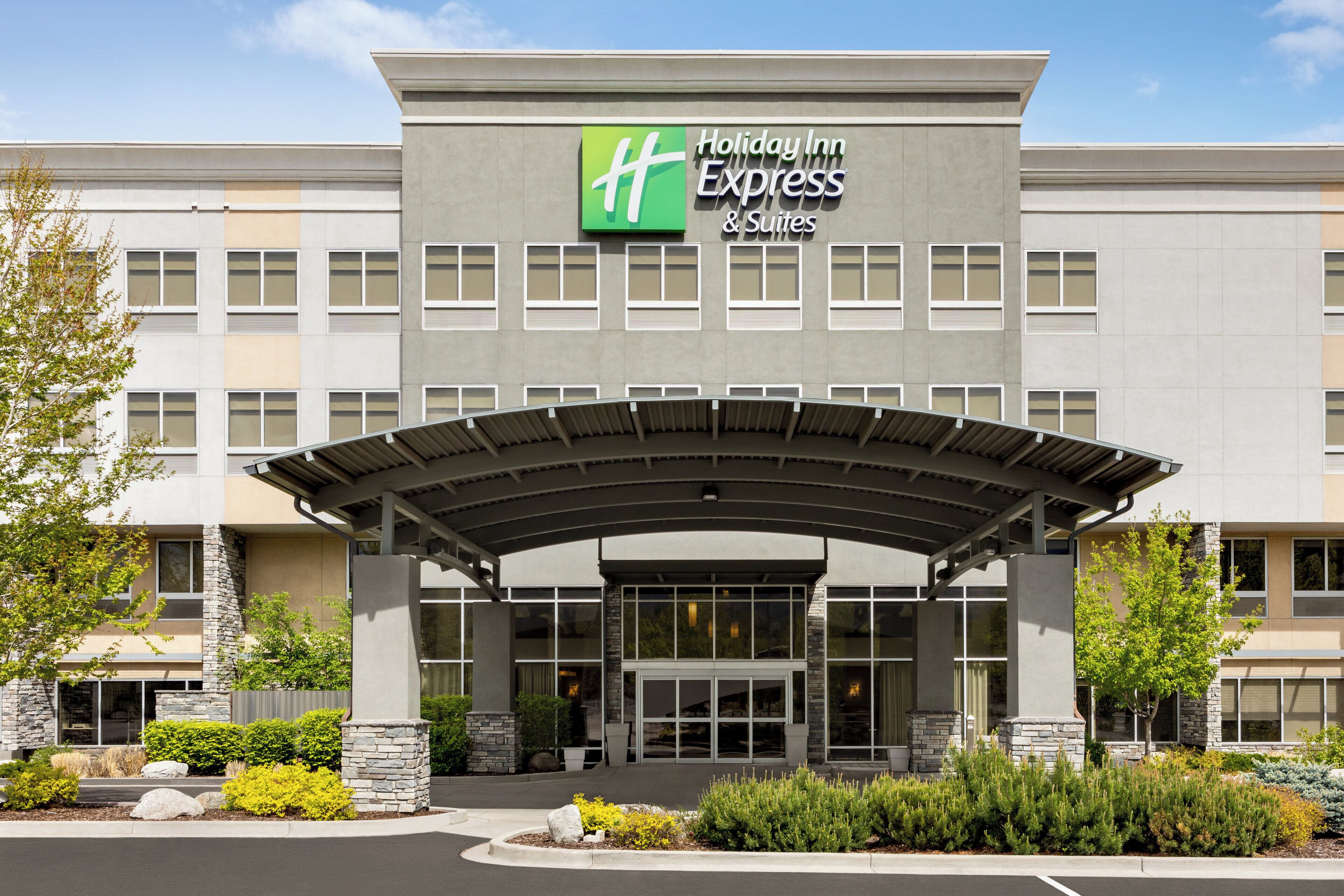 A Holiday Inn Express & Suites building with a covered entrance, stone pillars, and landscaped greenery.
