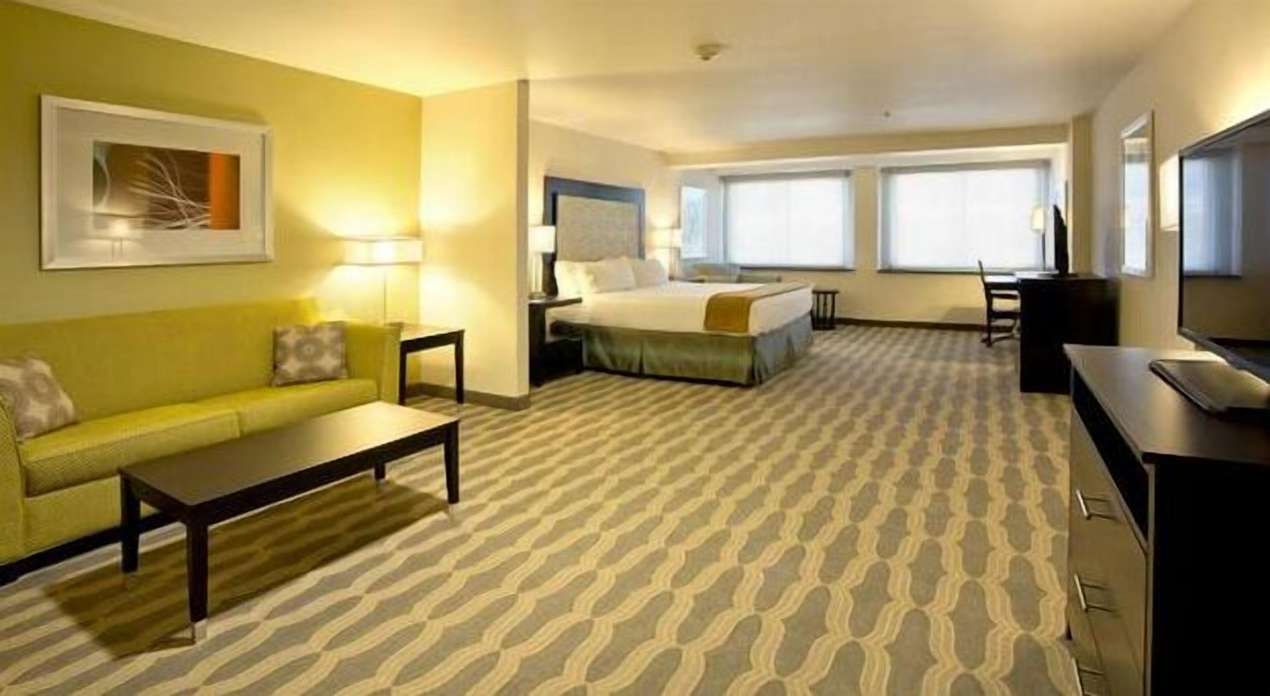 Ein Hotelzimmer mit Bett, einer Couch, einem Schreibtisch und einem Fernseher.