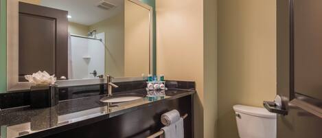 A bathroom with a black countertop, a white sink, a mirror, a toilet, and a towel rack.