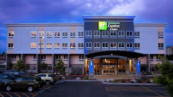 A Holiday Inn Express & Suites building with a modern design, featuring a large entrance and a parking lot with several cars.