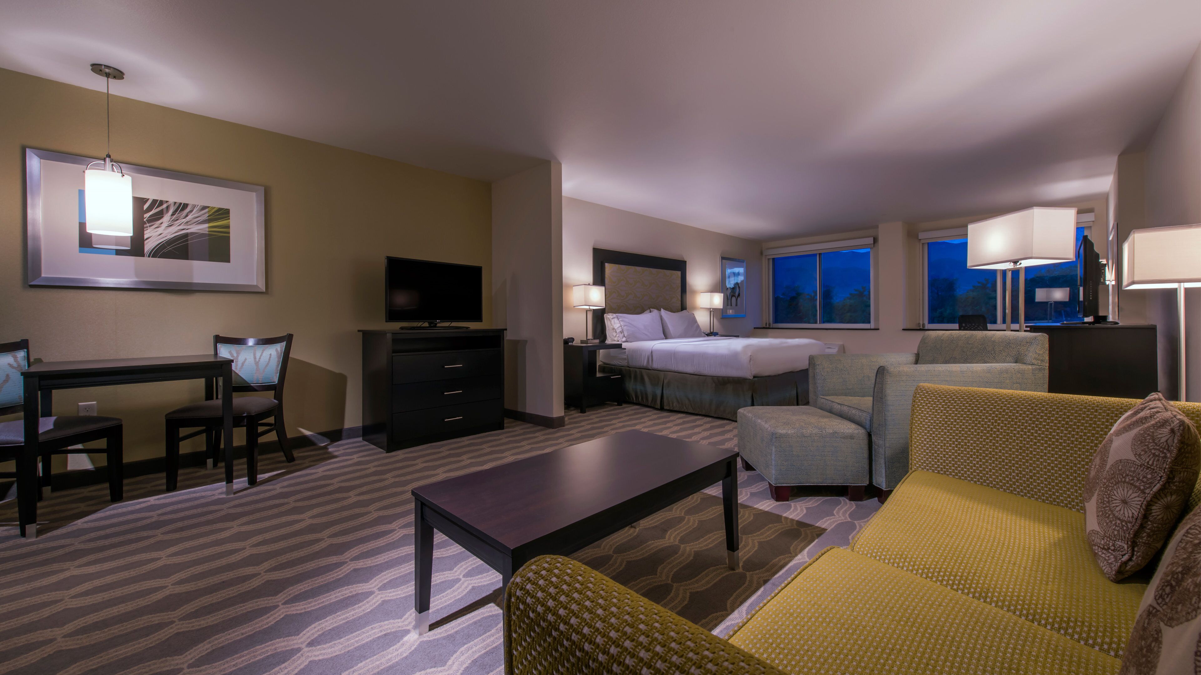 A hotel room with a bed, a sofa, a desk with a chair, a television, and a window with a view.