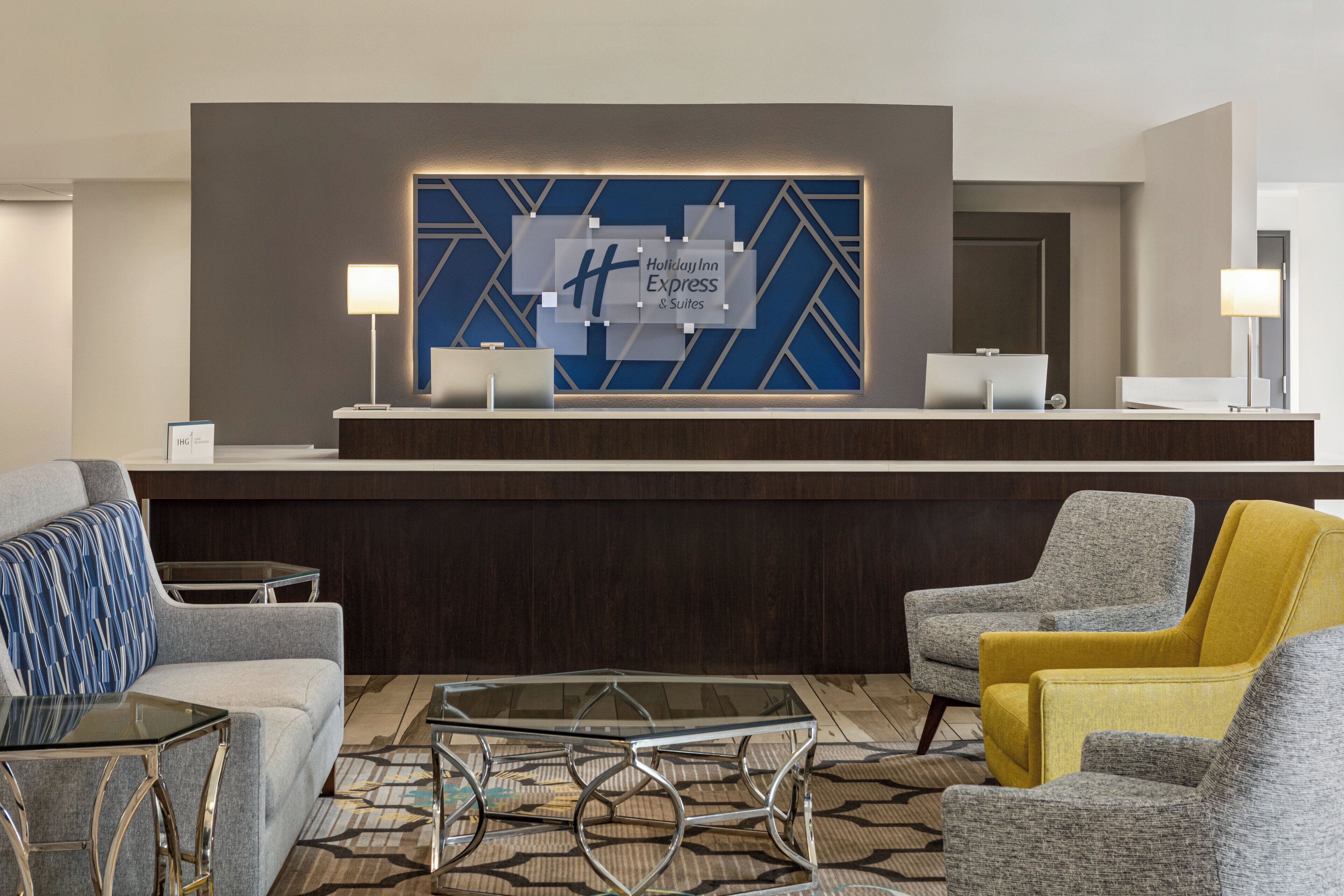 Zona de recepción de hotel con diseño moderno, que incluye un mostrador de recepción, un área de estar con sillones y una mesa de centro de vidrio.