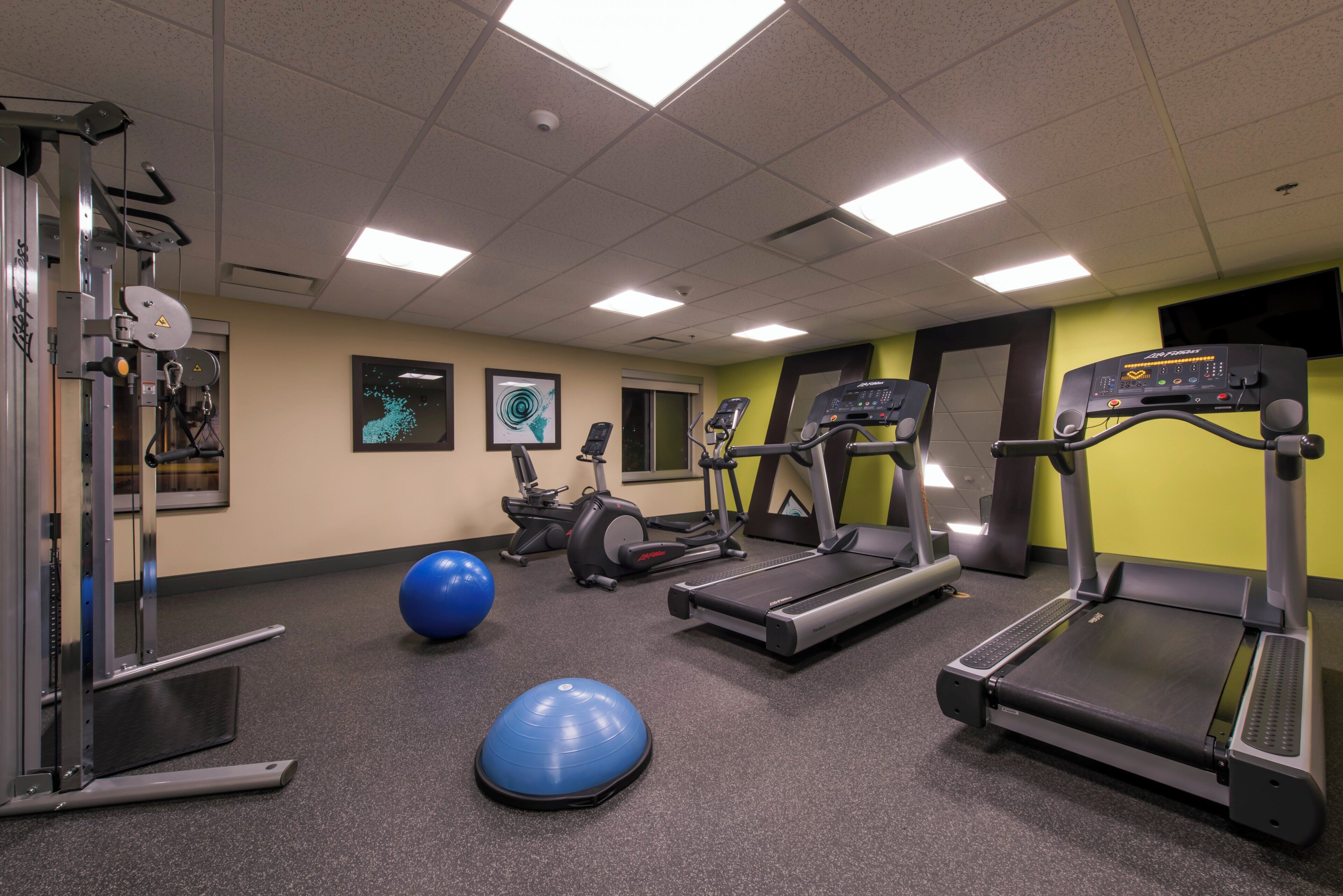 Une salle de sport équipée de tapis de course, de vélos elliptiques, d’un vélo d’appartement et de ballons d’exercice.