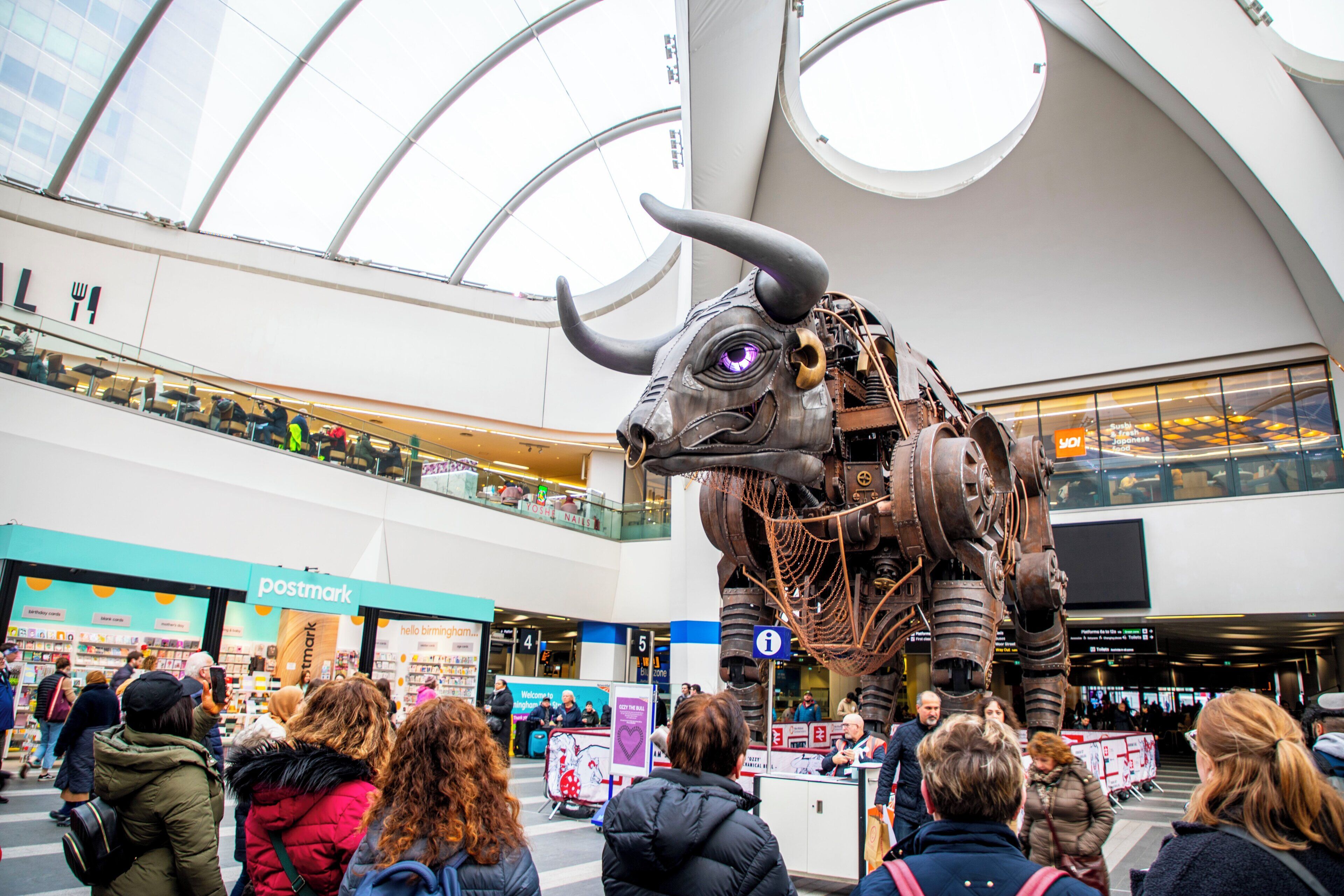 Una escultura de toro en un centro comercial, con gente observándola.
